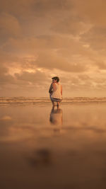 Man standing on beach against sky during sunset