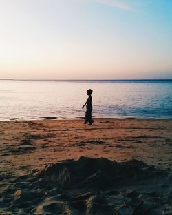 Silhouette woman walking at beach against sky during sunset