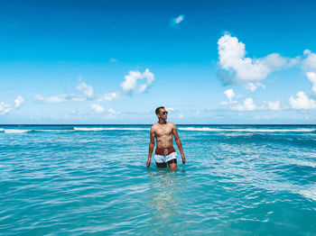 Full length of shirtless man in sea against sky