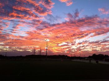 Silhouette trees on field against dramatic sky during sunset