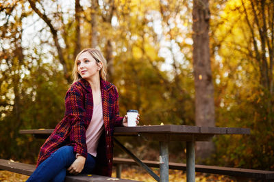 Young woman sitting on picnic table in park during autumn