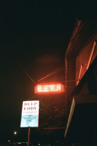 Low angle view of illuminated sign against sky at night