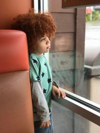 Boy with curly hair looking through window while standing at home