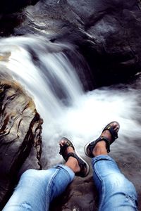 Low section of man sitting on rock by stream