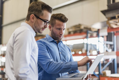 Two businessmen sharing laptop on factory shop floor