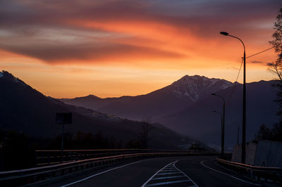 Road by mountains against sky during sunset