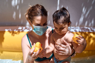 Young mother with a mask in an inflatable pool with her little daughter. safe holiday concept