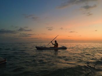 Man in sea against sky during sunset