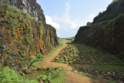 Dirt road amidst rocks and trees against sky