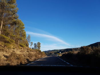 Road amidst trees against clear blue sky seen through car windshield