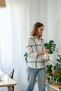 A young woman takes care of her houseplants gently by spraying them. home gardening concept.