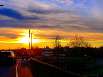 Cars on street against dramatic sky during sunset