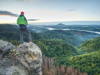 Man standing on rock looking at mountains against sky