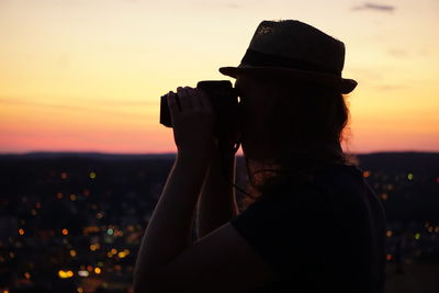 Rear view of woman photographing against sky during sunset