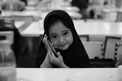 Portrait of smiling girl using phone sitting at restaurant
