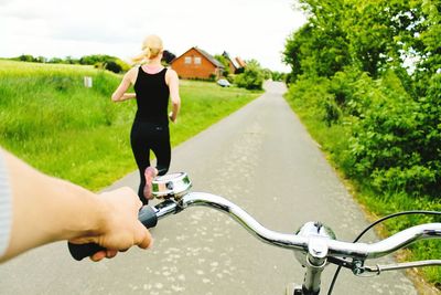 Cropped image of man riding bicycle on street with woman running in background