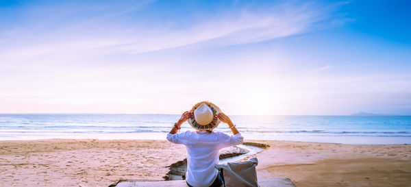 Rear view of woman standing at beach against sky