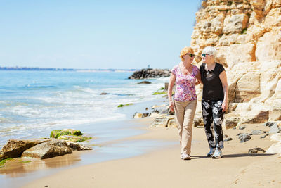 Two elderly women are walking along the rocky shore