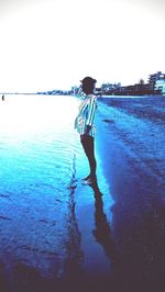 Rear view of boy standing in sea against clear sky