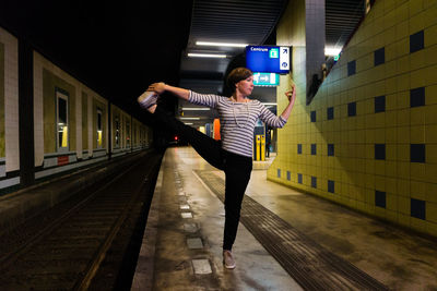 Woman standing on one leg at railroad station platform during night
