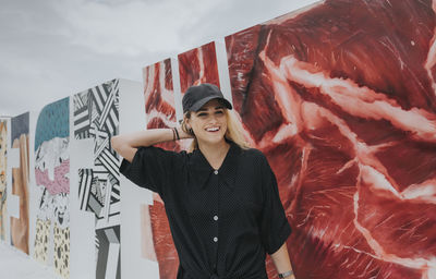 Portrait of smiling young woman standing against wall