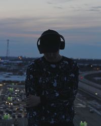 Man wearing headphones standing against sky during sunset