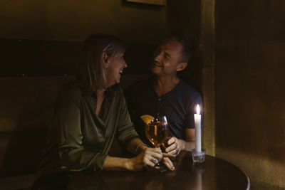 Happy mature couple enjoying candlelight date while having wine at restaurant