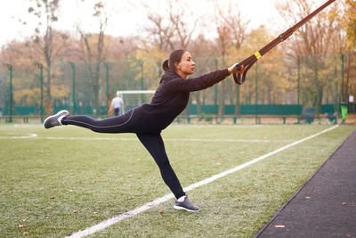 Side view of woman exercising with strap in public park