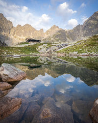 Alpine hut surrounded by mountains reflected in foreground tarn during sunrise, slovakia, europe