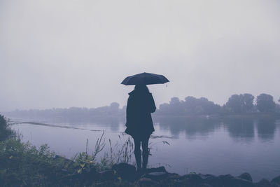 Silhouette woman standing by lake against sky