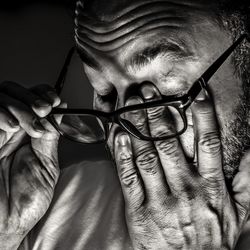 Close-up of man with eyeglasses rubbing eyes against black background