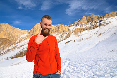 A man shows a goat gesture against the background of mountains with snow