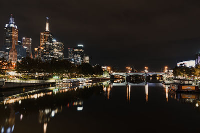 Illuminated buildings by river against sky at night