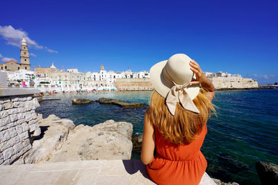 Woman sitting on the quay of monopoli port looking the historic town from seaview.