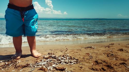 Low section of boy standing at dirty beach against sea