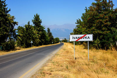 Road sign by trees against sky