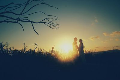 Man and woman standing on field against sky during sunset