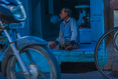 Side view of man sitting on blue car at night