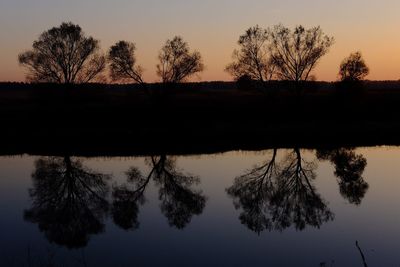 Silhouette trees by lake against sky during sunset