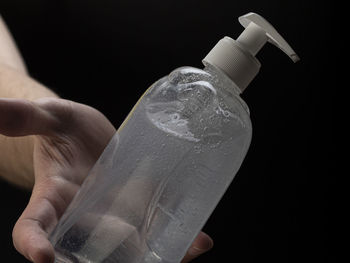 Close-up of hand holding bottle against black background