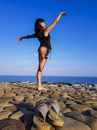 Side view of woman standing on one leg at beach