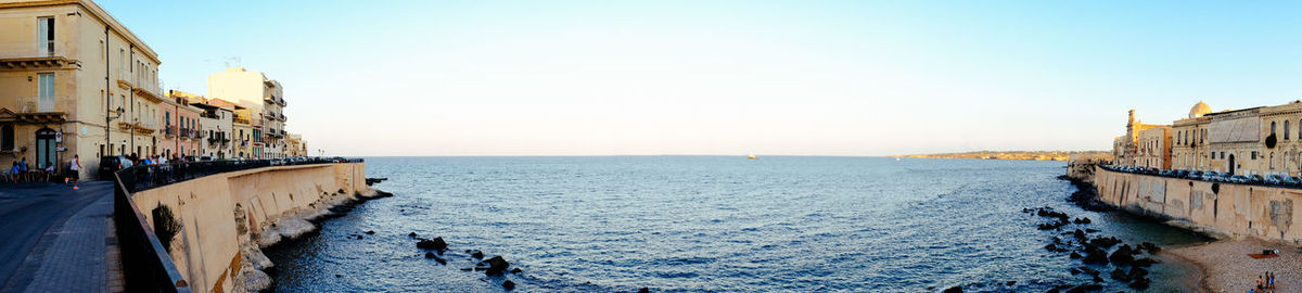 People on sea by buildings against clear sky