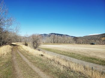 Empty road along landscape and mountains against clear blue sky