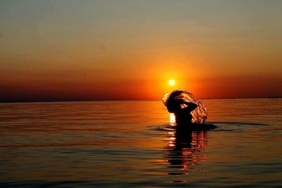 Silhouette woman tossing hair in sea against orange sky