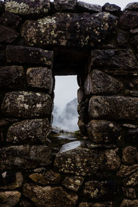 Stone wall by rocks against sky