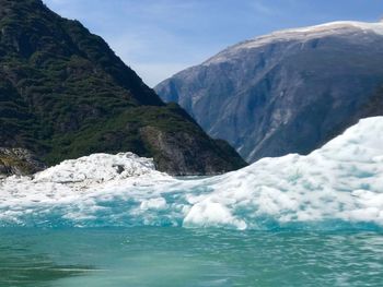 Scenic view of sea with iceberg by mountains against sky