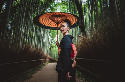 Side view of woman with umbrella standing amidst trees