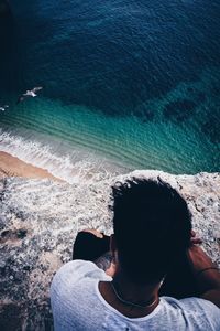 High angle view of man sitting on cliff by beach