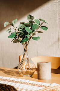 A vase with eucalyptus branches and a candle on the table.