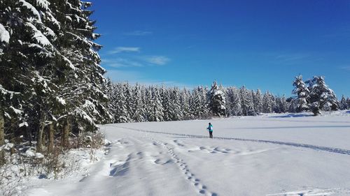 Man on snow covered field against blue sky